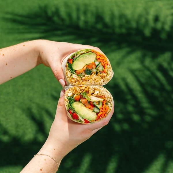 Hands holding a Diced healthy burrito, cut in half, filled with rice, avocado, and vegetables.