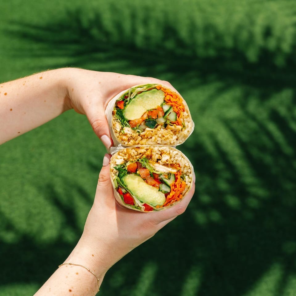 Hands holding a Diced healthy burrito, cut in half, filled with rice, avocado, and vegetables.