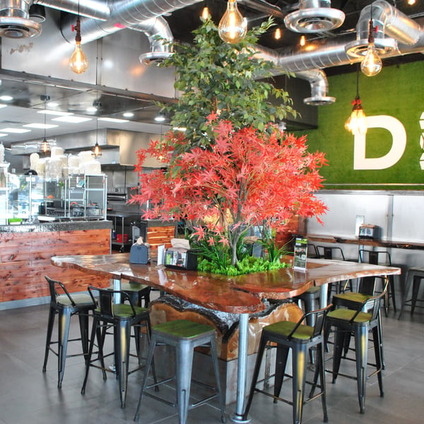 Diced restaurant interior with a large communal wooden table, bar stools, and a green wall with the Diced logo.