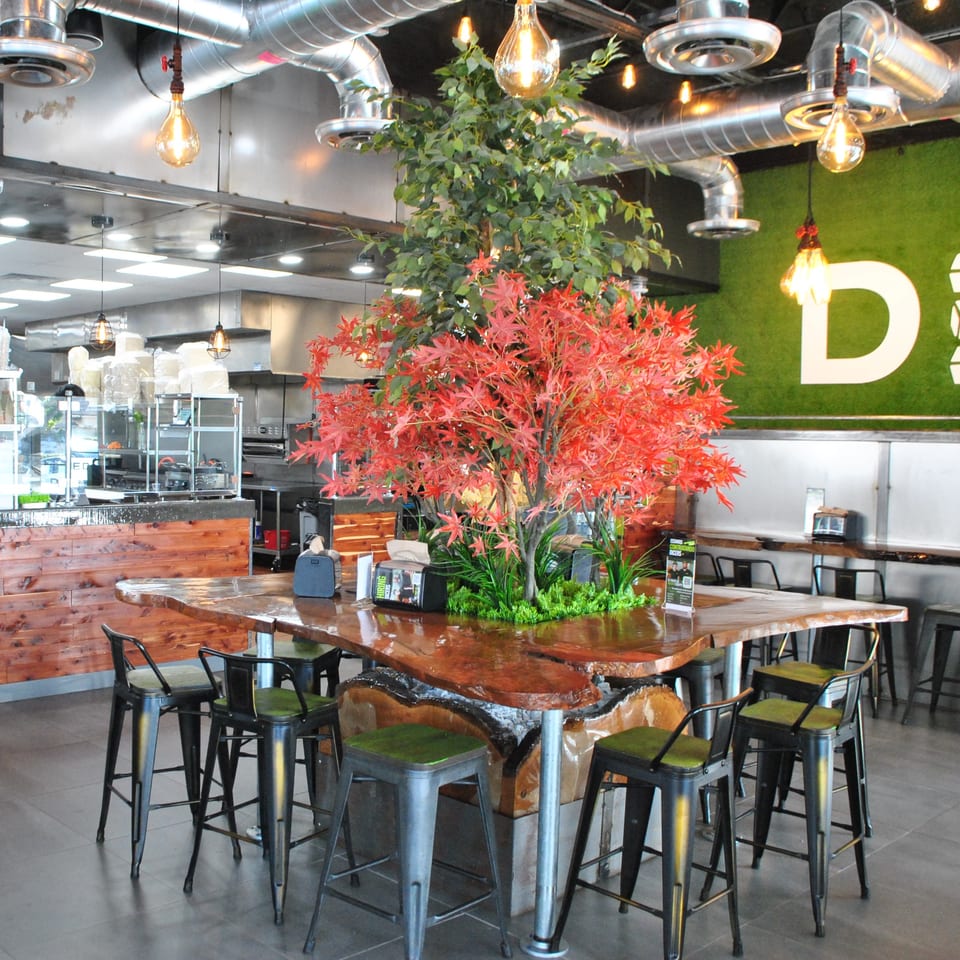 Diced restaurant interior with a large communal wooden table, bar stools, and a green wall with the Diced logo.