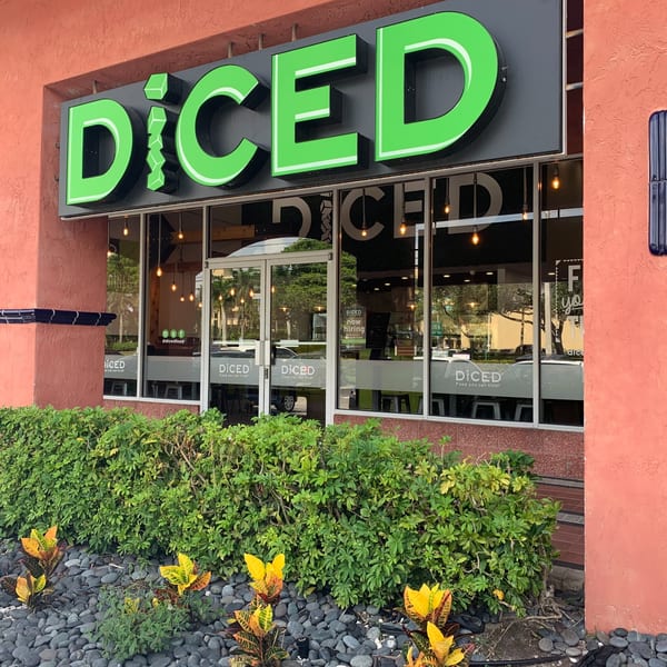 Exterior of Diced restaurant with a bright green sign, large windows, and lush landscaping.