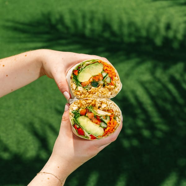 Hands holding a Diced healthy burrito, cut in half, filled with rice, chicken, avocado, and vegetables.