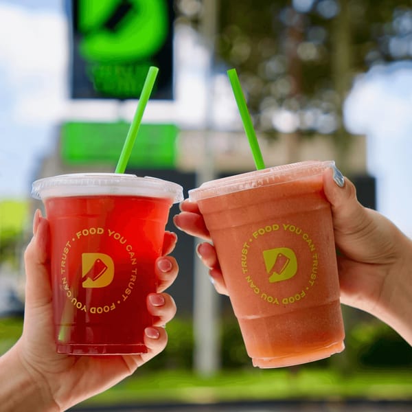 Two hands hold up Diced branded drinks, one red and one orange, with green straws.