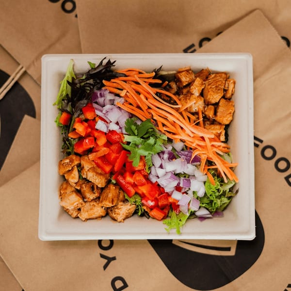 A Diced healthy salad with chicken, red peppers, carrots, and onions in a compostable container.
