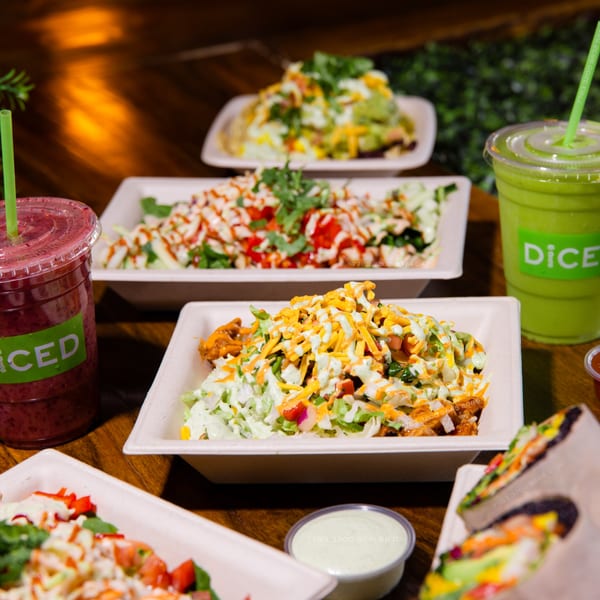 Multiple Diced healthy bowls with fresh ingredients and two smoothies on a wooden table.
