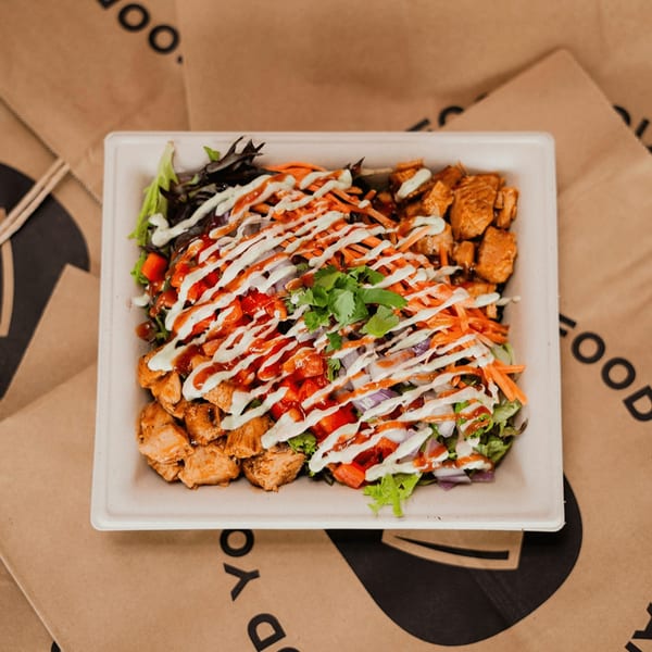 Diced healthy bowl with chicken, lettuce, carrots, tomatoes, and sauces on a brown paper bag.