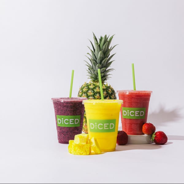 Three Diced smoothies in purple, yellow, and red, with pineapple, pineapple chunks, and strawberries.