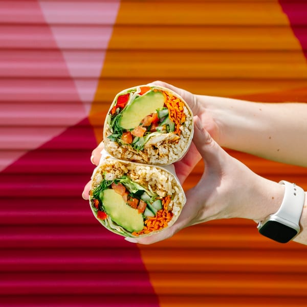Hands hold a Diced healthy burrito, sliced in half, revealing avocado, chicken, rice, and vegetables.
