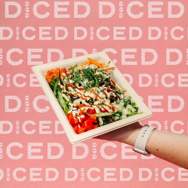 A hand holding a Diced healthy salad bowl with mixed greens, vegetables, and two sauces.