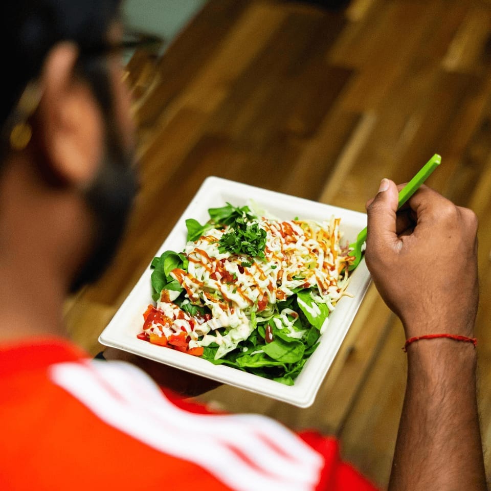 A person in a red shirt eating a Diced healthy salad with various toppings and dressings.