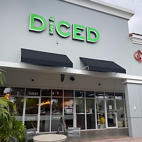 Exterior view of Diced restaurant, featuring its green logo, black awnings, and outdoor seating.