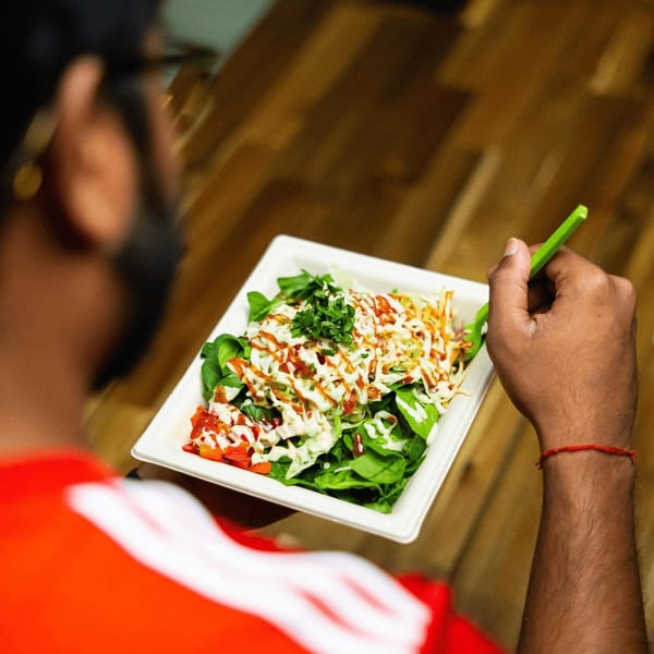 A person in a red shirt eating a Diced healthy salad with various toppings and dressings.
