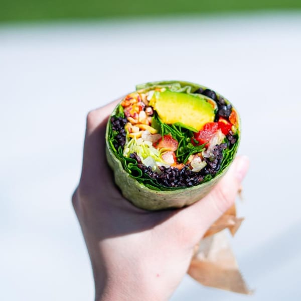 A hand holds a Diced healthy wrap filled with black beans, avocado, and fresh vegetables.