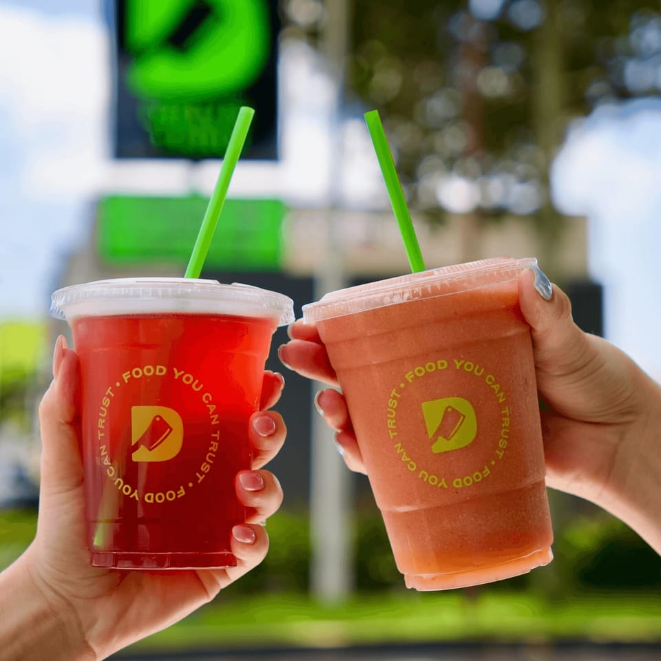 Two hands hold up Diced branded drinks, one red and one orange, with green straws.