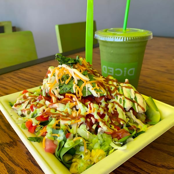 A Diced salad with various toppings and dressings, alongside a green smoothie on a wooden table.