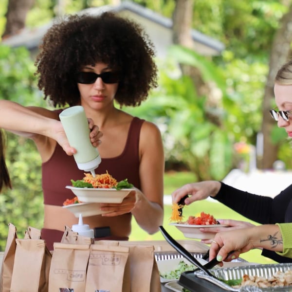 People serving themselves healthy Diced bowls with various toppings at an outdoor event.