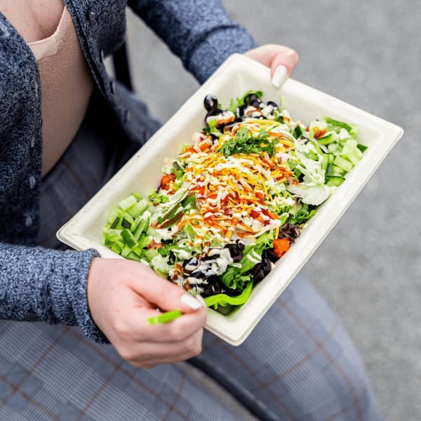A person holds a Diced healthy salad in a rectangular container, with a green fork ready to eat.