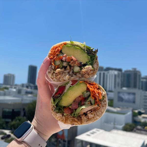 A hand holds a Diced healthy burrito, cut in half, against a city skyline under a blue sky.