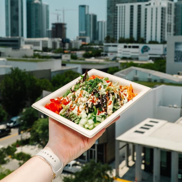 A hand holds a Diced healthy salad bowl with dressing, against a city skyline backdrop.