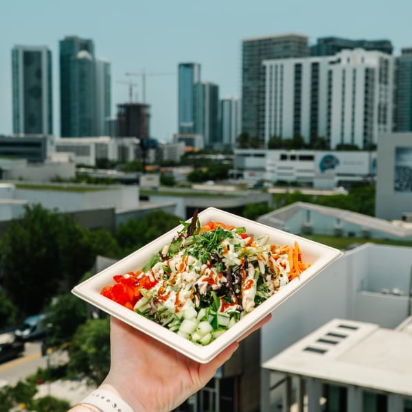 A hand holds a Diced healthy salad bowl with a city skyline in the background.