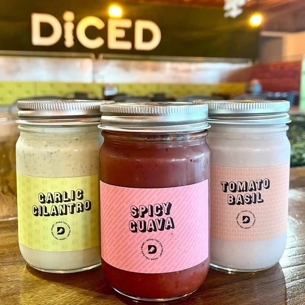 Three Diced brand sauce jars: Garlic Cilantro, Spicy Guava, and Tomato Basil, on a wooden table.