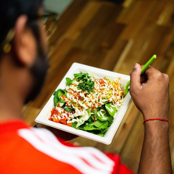 A person in a red shirt holds a Diced salad with green lettuce, red tomatoes, and white dressing.
