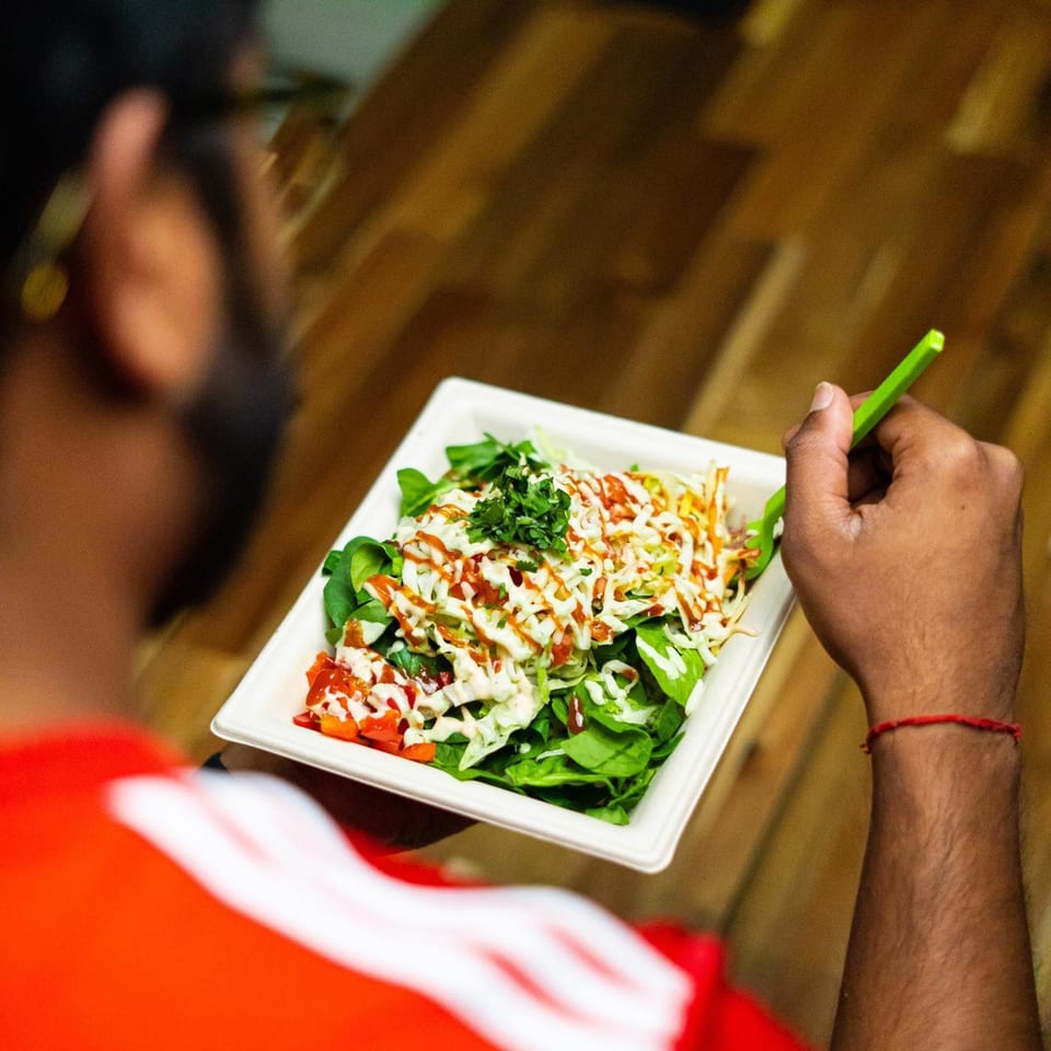 A person in a red shirt holds a Diced salad with green lettuce, red tomatoes, and white dressing.