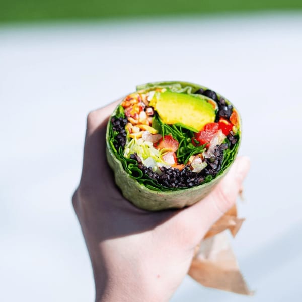 A hand holds a vibrant Diced healthy wrap, filled with avocado, black beans, and fresh vegetables.
