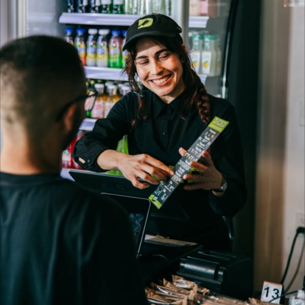 A smiling Diced employee in a cap shows a menu to a customer at the counter.