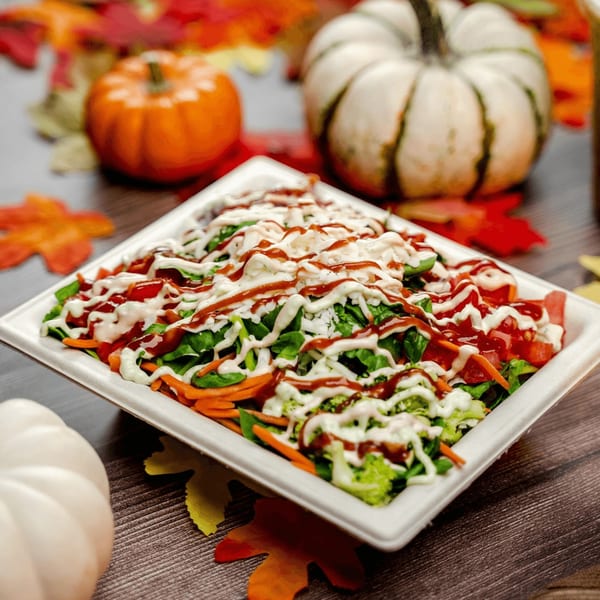 A Diced healthy salad with dressing, surrounded by autumn leaves and pumpkins.